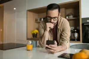 A man leaning on the kitchen counter while on his phone.